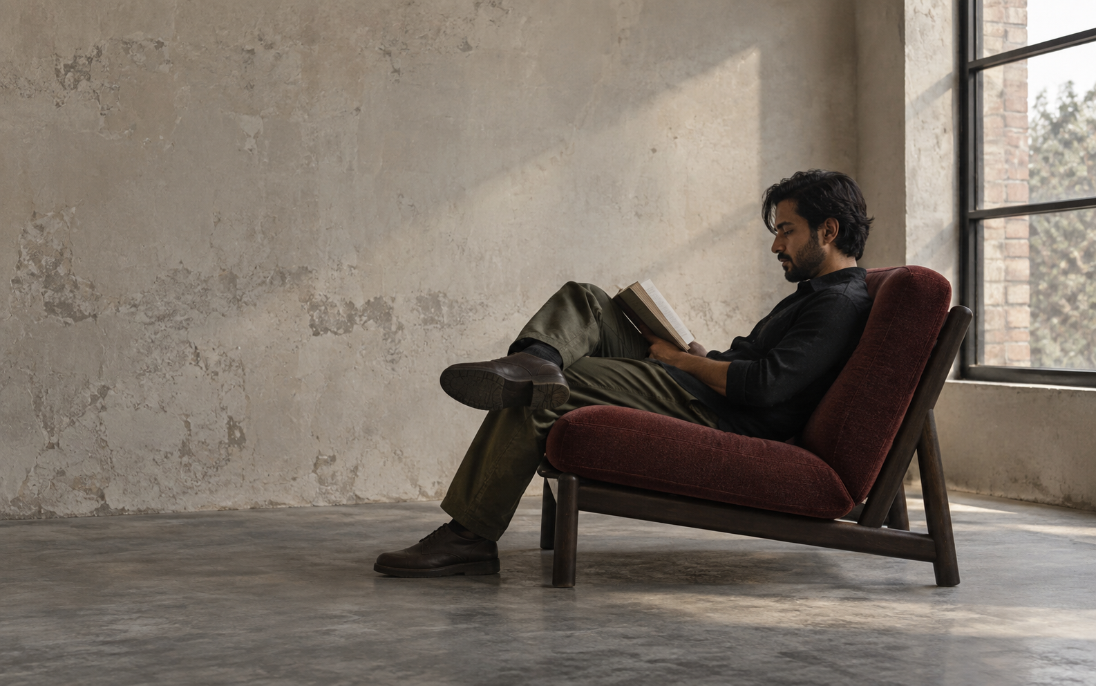 A reader settled into a deep oxblood lounge chair in a quiet studio